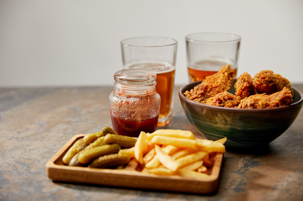 delicious chicken nuggets, french fries and gherkins near glasses of beer on stone surface isolated on grey - Zdjęcie, obraz