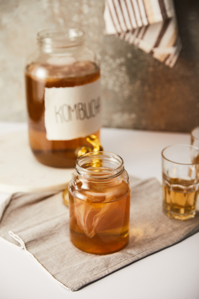 selective focus of jar with kombucha near glasses on textured grey background with striped napkin - 写真・画像