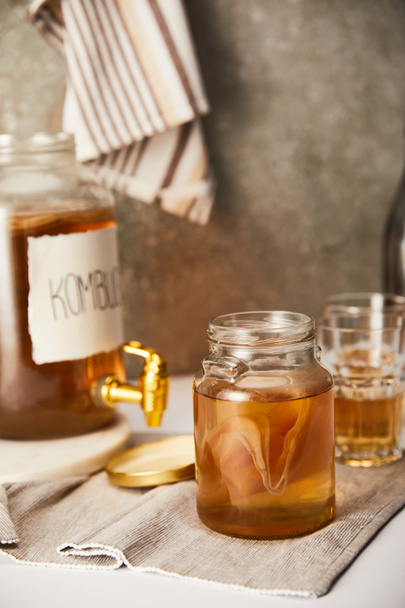 selective focus of jar with kombucha near glasses on textured grey background with striped napkin - Photo, Image