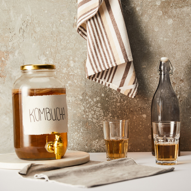 jar with kombucha near glasses on textured grey background with striped napkin - Foto, afbeelding