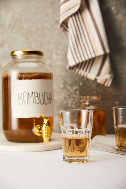 selective focus of jar with kombucha near glasses on textured grey background with striped napkin - Fotoğraf, Görsel