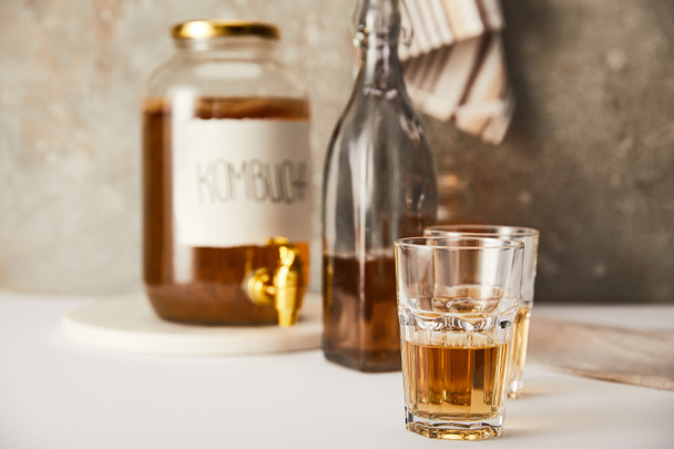 selective focus of jar with kombucha near glasses and bottle on textured grey background with striped napkin - 写真・画像