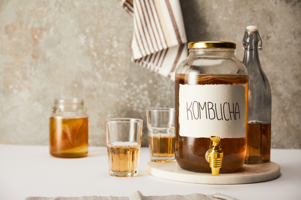 jar with kombucha near glasses and bottle on textured grey background with striped napkin - Фото, изображение