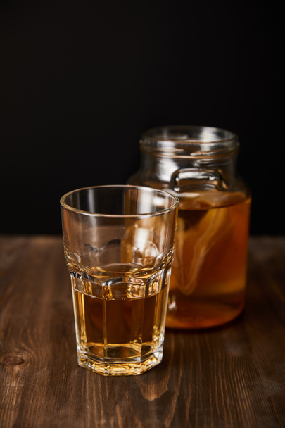 glass and jar with kombucha on wooden table isolated on black - Photo, Image
