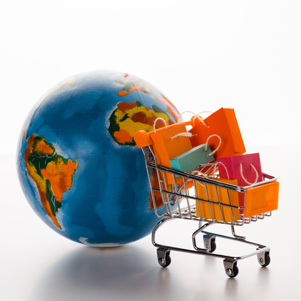 carrito de compras de juguete con bolsas de compras cerca del mundo en blanco, concepto de comercio electrónico
 - Foto, imagen