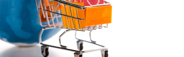 panoramisch shot van speelgoedwinkelwagentje met boodschappentassen bij wereldbol op wit, e-commerce concept - Foto, afbeelding