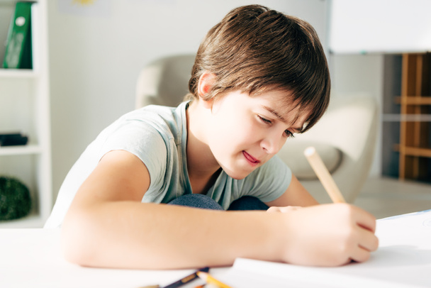 kid with dyslexia drawing with pencil and sitting at table  - Foto, Imagen