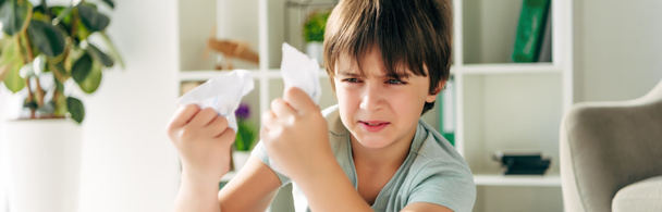 Okuma zorluğu çeken ve elinde buruşuk kağıtlar tutan sinirli bir çocuğun panoramik görüntüsü.  - Fotoğraf, Görsel