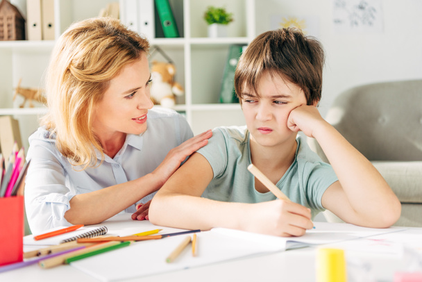 sad kid with dyslexia holding pencil and smiling child psychologist talking to him  - Фото, изображение