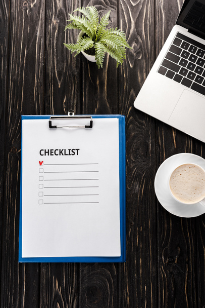 top view of clipboard with checklist near laptop, plant, red marker pen and cup of coffee on table, e-commerce concept - Fotoğraf, Görsel