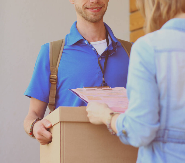 Smiling delivery man in blue uniform delivering parcel box to recipient - courier service concept. Smiling delivery man in blue uniform - Foto, afbeelding