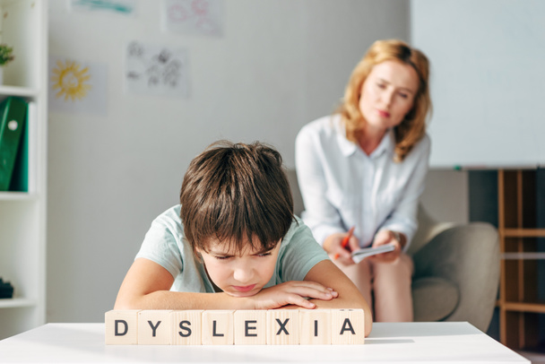 enfoque selectivo de niño triste con dislexia sentado en la mesa con cubos de madera con letras dislexia
 - Foto, imagen