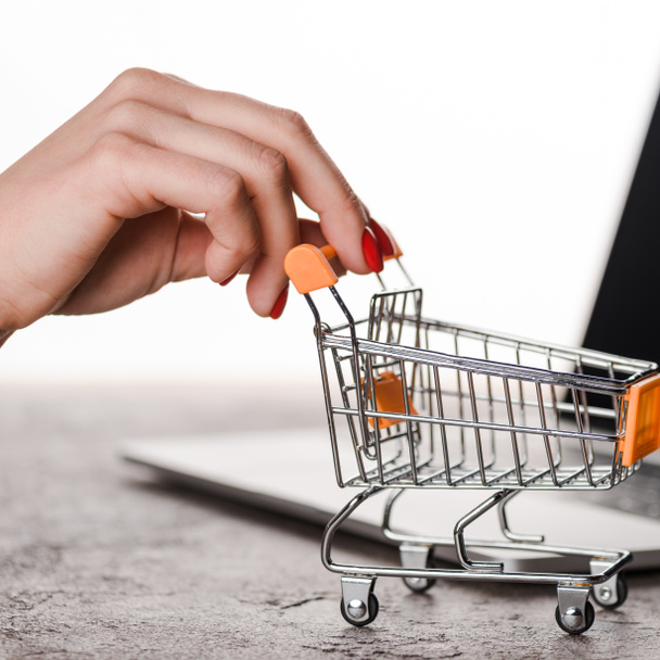close up of woman holding toy shopping cart near laptop isolated on white, e-commerce concept - 写真・画像