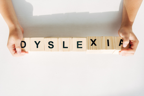 cropped view of kid with dyslexia holding wooden cubes with lettering  - Foto, Imagen