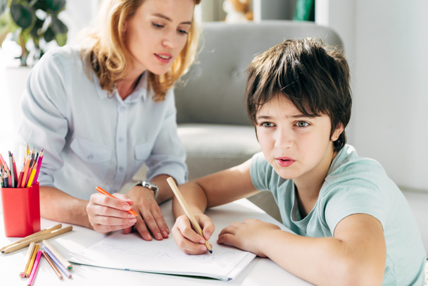 ребенок с дислексией и детский психолог сидит за столом и держит карандаши
  - Фото, изображение