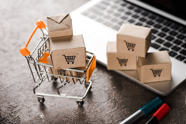 selective focus of toy shopping cart with small carton boxes near laptop, e-commerce concept - Photo, Image
