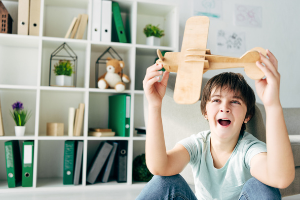roztomilé dítě s dyslexií zívání a hraní s dřevěným letadlem  - Fotografie, Obrázek