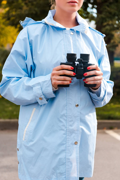 vista recortada de la mujer en impermeable azul con prismáticos
  - Foto, Imagen