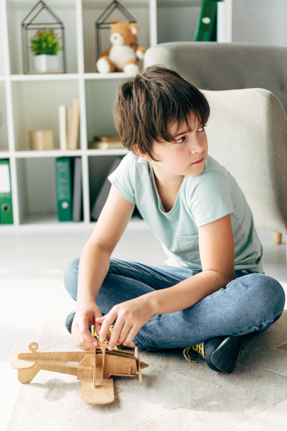 kid with dyslexia sitting on floor and holding wooden plane  - Foto, Imagen