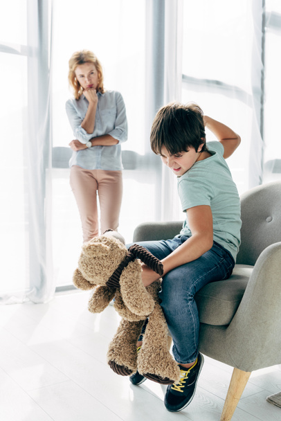 сердитий дитина з дислексією гладить плюшевого ведмедя і дитячий психолог дивиться на нього
  - Фото, зображення