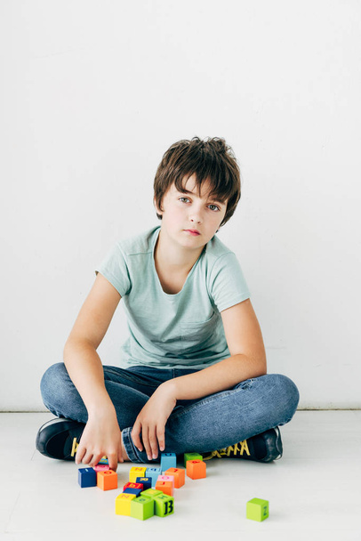 dítě s dyslexií sedí na podlaze s stavebními kameny na bílém pozadí  - Fotografie, Obrázek