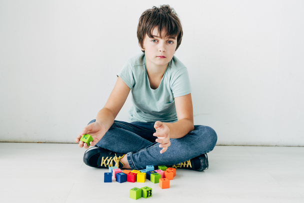 kid met dyslexie zittend op de vloer met bouwstenen op witte achtergrond  - Foto, afbeelding