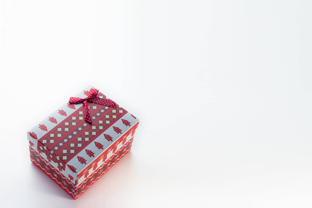 eine rote weihnachtsschachtel mit geschenken und schleife steht auf weißem grund mit einem platz für postkartentext schräg links. Auf der Schachtel liegen Weihnachtsbäume und Schneeflocken. - Foto, Bild