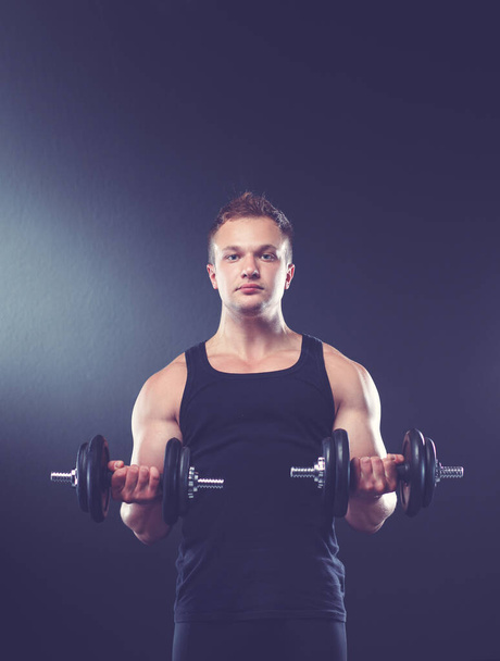 young man exercising with dumbbells on dark background - Fotoğraf, Görsel