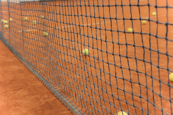 Tennisballen op rode baan met grijs net - Foto, afbeelding