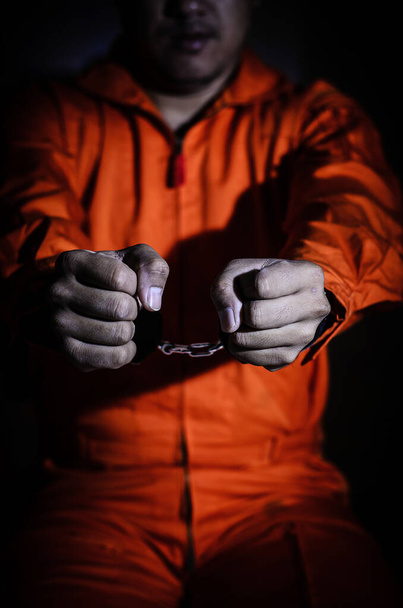 the bottom body part of the prisoner in orange uniform holding hands in handcuffs front of him  - Foto, Imagem