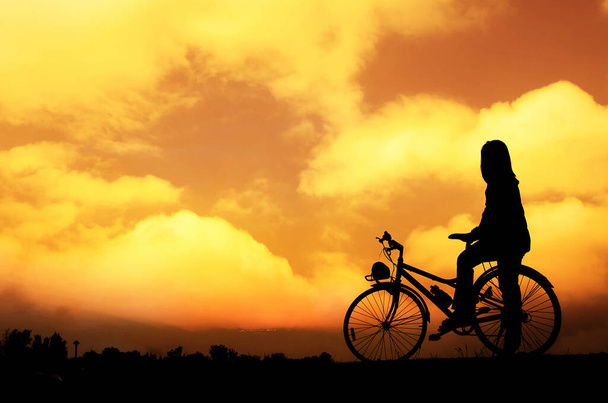 silhouette of the unrecognizable girl with bicycle at sunset with beautiful clouds and horizon   - Фото, зображення