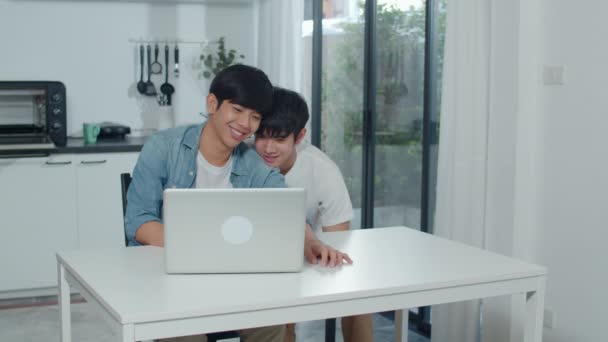 Fiatal meleg pár számítógépes laptoppal a modern otthonban. Ázsiai Lgbtq férfiak boldog pihenjen szórakoztató technológia segítségével filmet nézni az interneten együtt, miközben ül asztal konyha ház koncepció. - Felvétel, videó