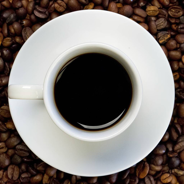 High angle shot of a white cup of black coffee on a surface full of coffee beans - Foto, immagini