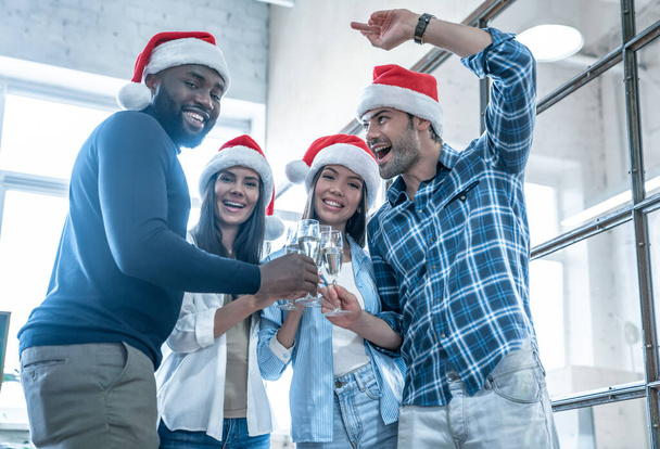 Boldog Karácsonyt és Boldog Új Évet 2020-ban. Multiracionális fiatal kreatív emberek ünneplik a nyaralást a modern irodában. Fiatal üzletemberek csoportja pezsgőt iszik munka közben. Sikeres. - Fotó, kép