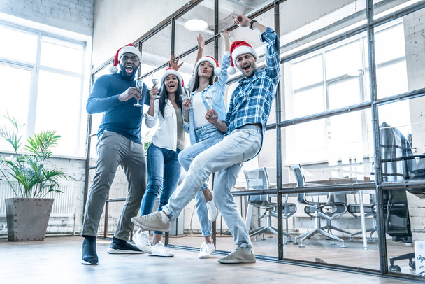 Mutlu Noeller ve mutlu yıllar 2020. Çok ırklı genç yaratıcı insanlar modern ofiste bayramı kutluyorlar. Bir grup genç iş adamı birlikte çalışarak şampanya içiyor. Başarılı. - Fotoğraf, Görsel