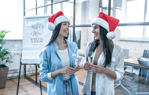 Merry Christmas and Happy New Year 2020.Young creative people are celebrating holiday in modern office. Young business women is drinking champagne in coworking. Successful hipster team of freelancers. - Photo, Image