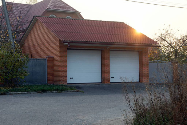 garaje de ladrillo marrón con dos puertas blancas en la calle por la carretera
 - Foto, Imagen