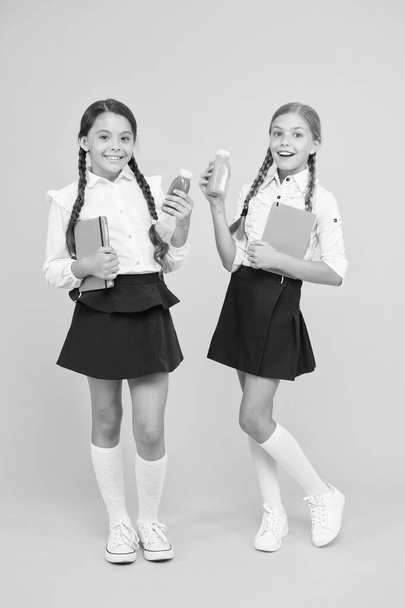Thirst and dehydration. Healthy snack fruit smoothie. Smoothie detox. Yummy smoothie. Healthy nutrition. Schoolgirls holding juice bottle on yellow background. Quenching thirst during school time - Zdjęcie, obraz