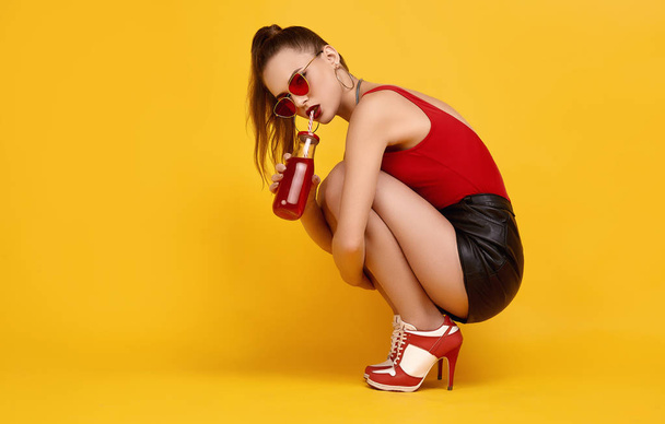 Elegant glamor hipster girl in red top, black shorts with cocktail drink - Fotó, kép