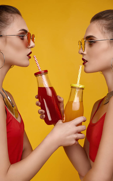 Two elegant glamor hipster twin girls in fashion red top with cocktail drink - Фото, изображение