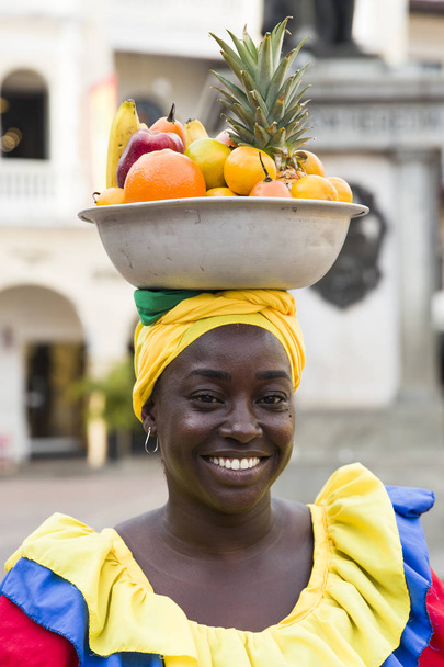 CARTAGENA, COLOMBIA - 16 сентября 2019 года: Неопознанная паленкера, продавщица фруктов на улице Картахена, Колумбия. Эти афро-колумбийские женщины родом из деревни Сан-Базилио-де-Паленке, недалеко от города
. - Фото, изображение
