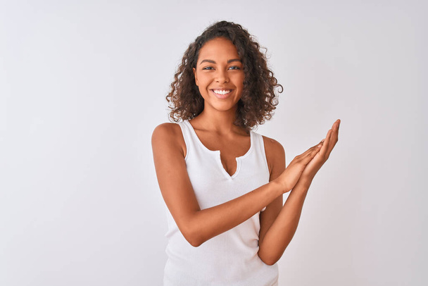 Mujer brasileña joven con camiseta casual de pie sobre fondo blanco aislado aplaudiendo y aplaudiendo felices y alegres, sonriendo orgullosas manos juntas
 - Foto, Imagen
