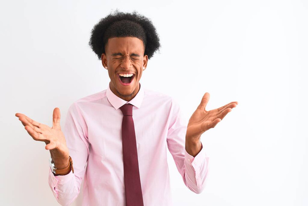 Genç Afrikalı Amerikalı iş adamı, izole edilmiş beyaz arka planda duran kravat takıyor ve kollarını kaldırıp heyecanla haykırarak başarının çılgınlığını kutluyor. Kazanan konsept - Fotoğraf, Görsel