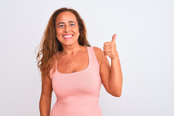 Middle age mature woman standing over white isolated background doing happy thumbs up gesture with hand. Approving expression looking at the camera with showing success. - Photo, Image