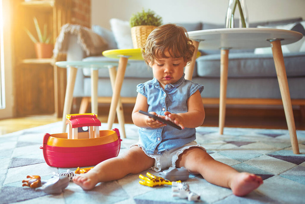 Beautiful toddler child girl sitting on the carpet playing with smartphone - 写真・画像