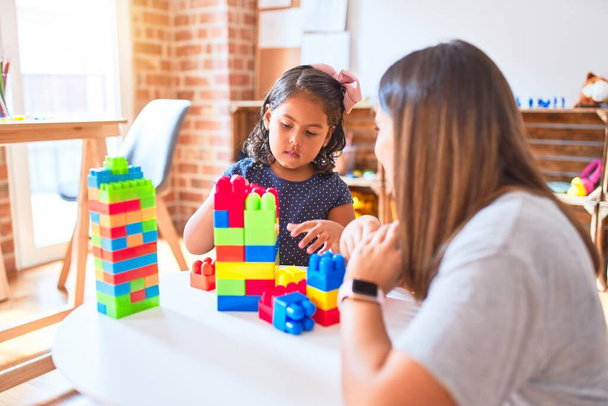 Hermosa maestra y niña jugando con bloques de construcción torre de construcción en el jardín de infantes
 - Foto, imagen