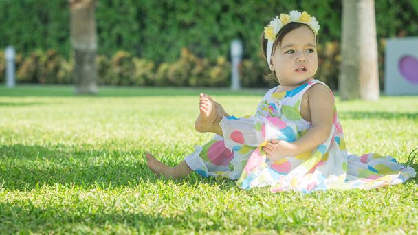 Little girl in colorful dress sitting on the grass - Fotoğraf, Görsel