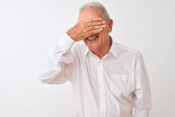 Старший сіро-волохатий чоловік в елегантній сорочці стоїть над ізольованим білим тлом, посміхаючись і сміючись рукою на обличчі, прикриваючи очі сюрпризом. Сліпа концепція
. - Фото, зображення