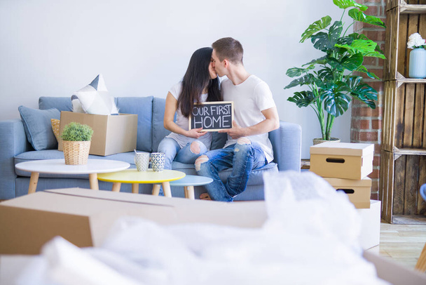 Молодая красивая пара сидит на диване держа доску с сообщением в новом доме вокруг картонных коробок
 - Фото, изображение