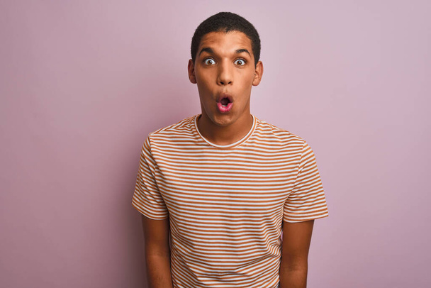 Young handsome arab man wearing striped t-shirt standing over isolated pink background afraid and shocked with surprise expression, fear and excited face. - Photo, Image